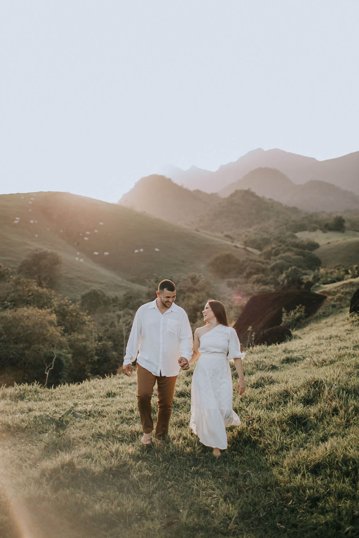 Homem com calça caqui e camisa branca e mulher com vetsido branco na montanha