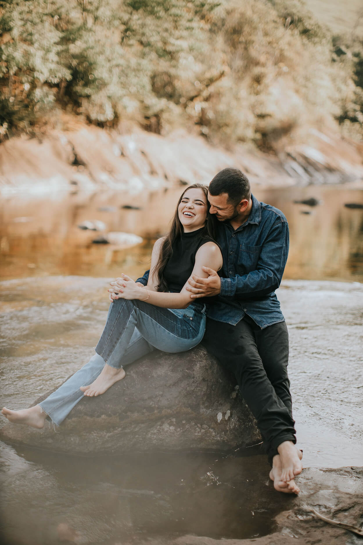 Casal se abraçando sobre pedra perto da cachoeira