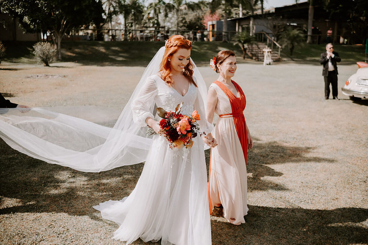 Noiva e mãe da noiva com vestido creme e laranja de mãos dadas