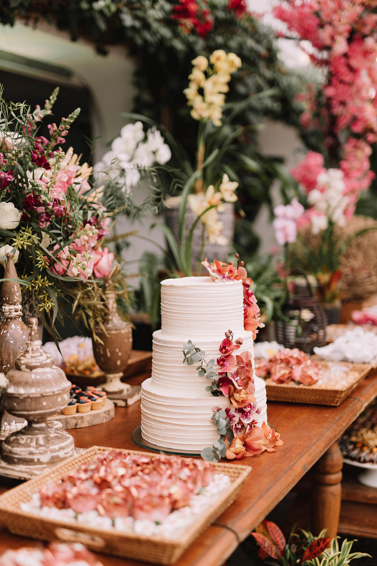 Mesa com bolo de casamento de três andares com folhas de eucalipto e orquídeas