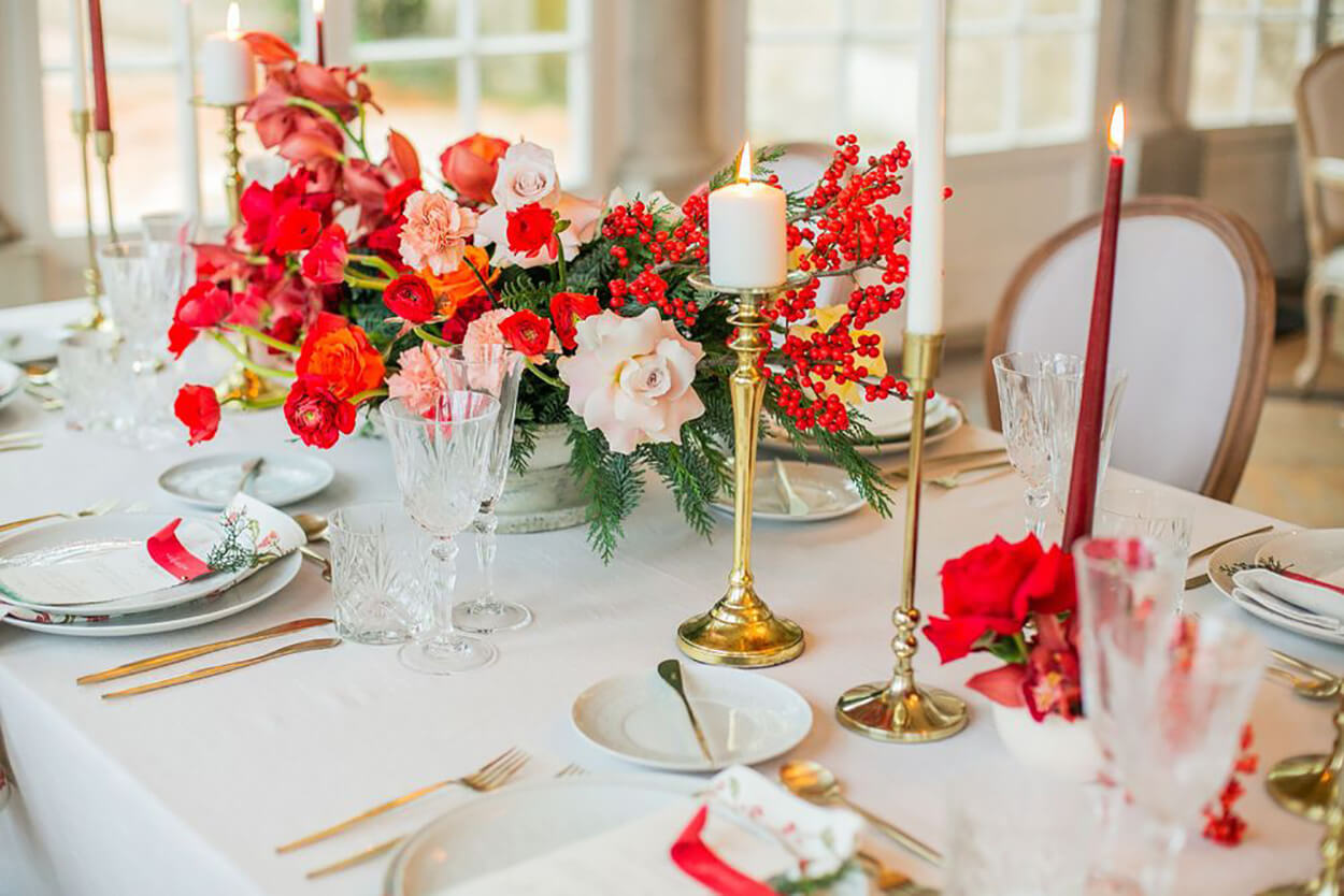 Mesa postas com castiçais dourados, velas vermelhas e brancas com flores no centro