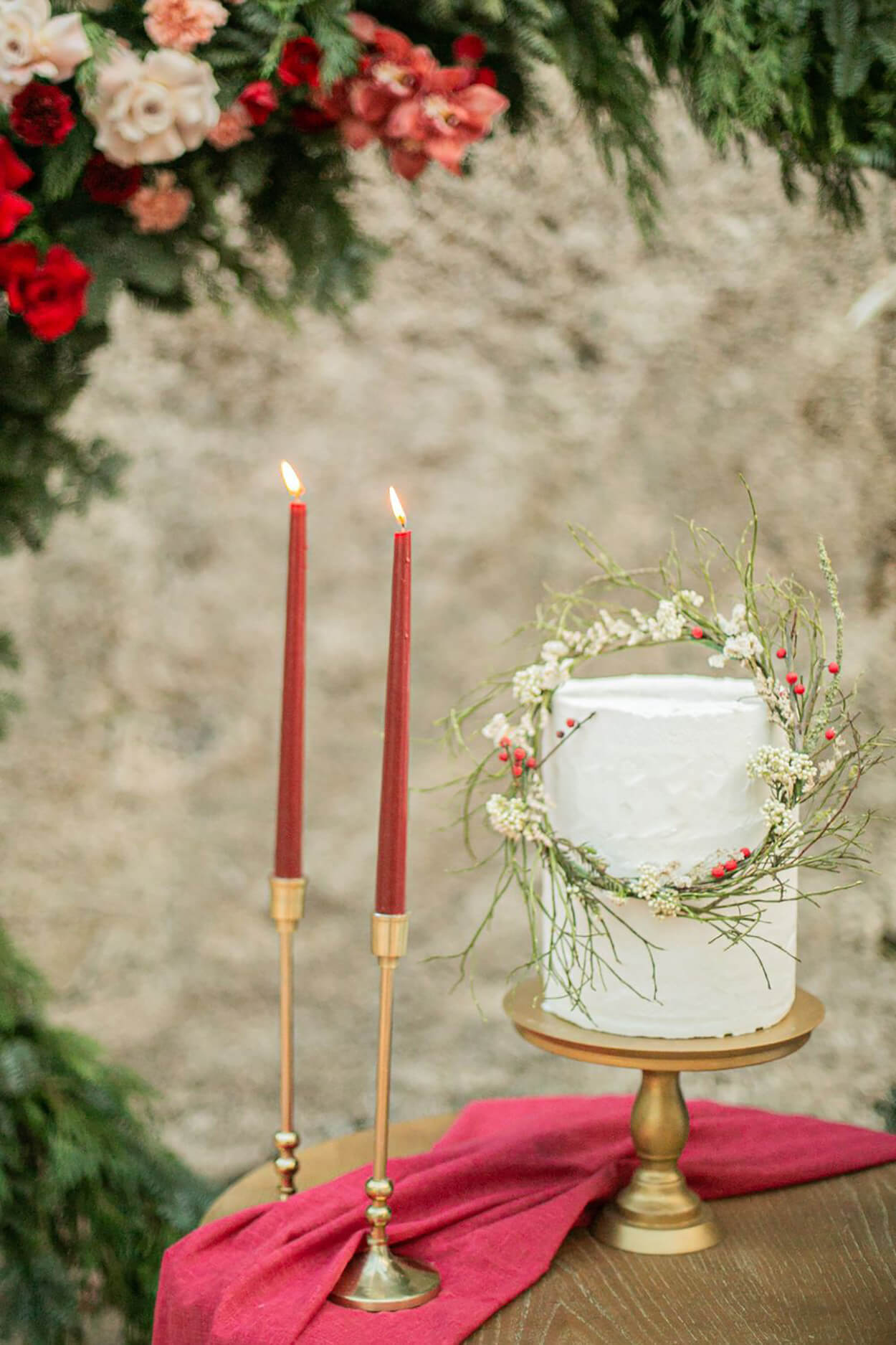 Bolo de casamento branco com dois andares com coroa de flores e castiçais com velas vermelhas
