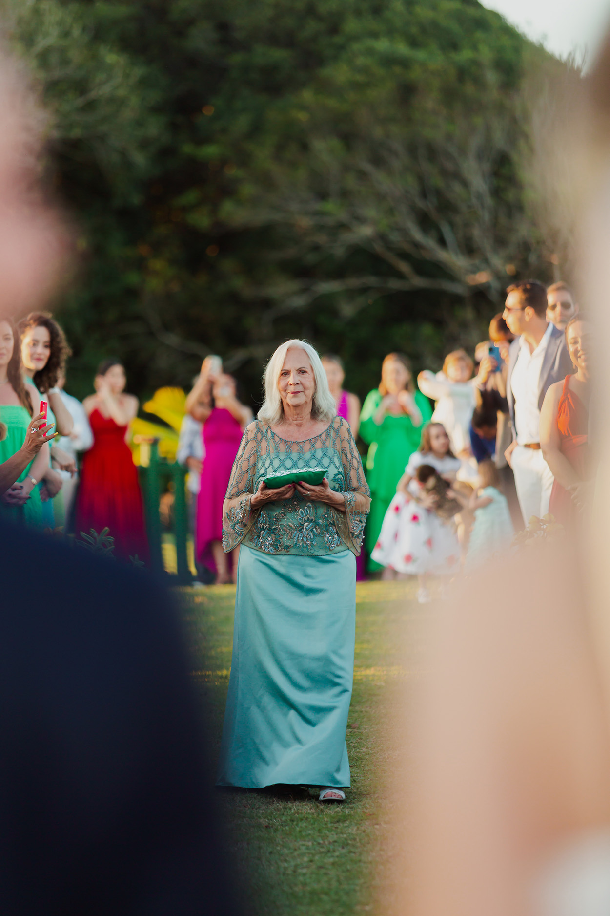 Senhora com vestido azul turquesa carregando almofada com porta alianças