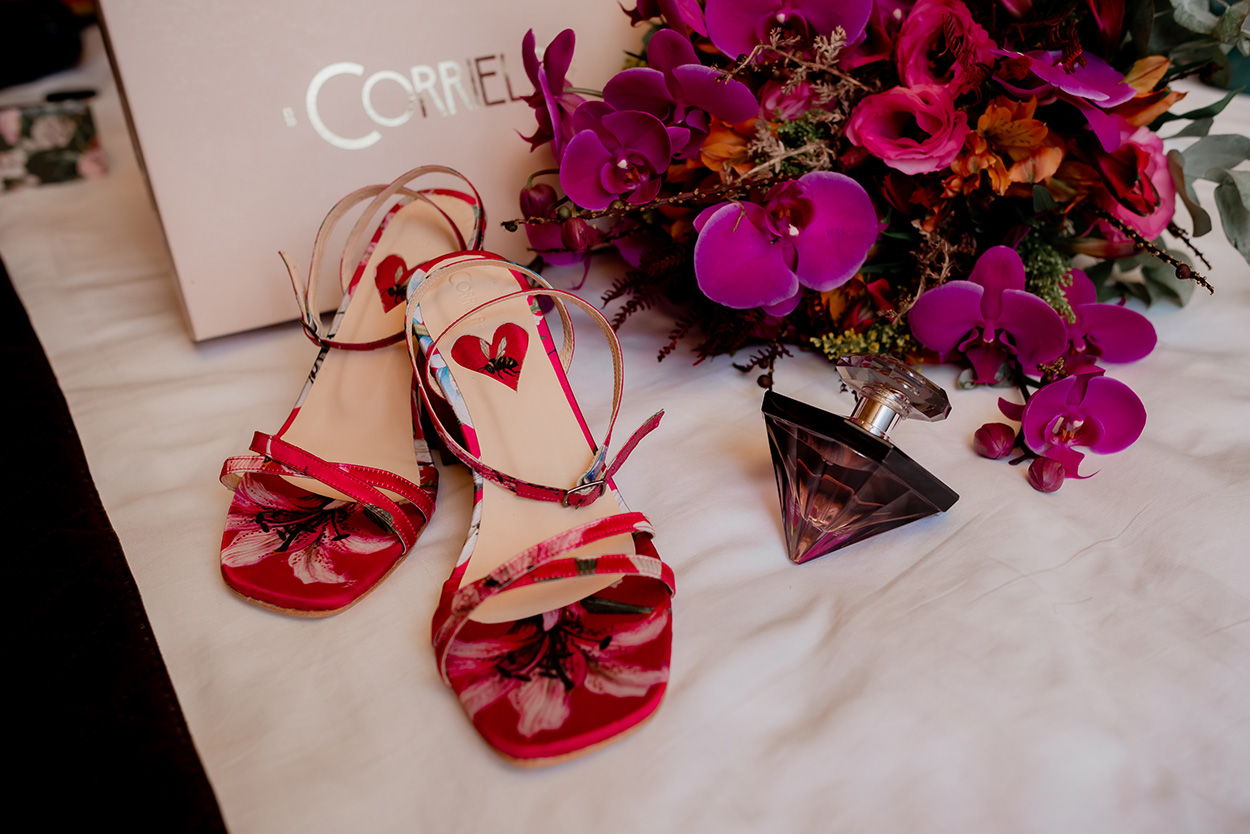 Sandália vermelha, perfume e buquê com orquídeas roxas