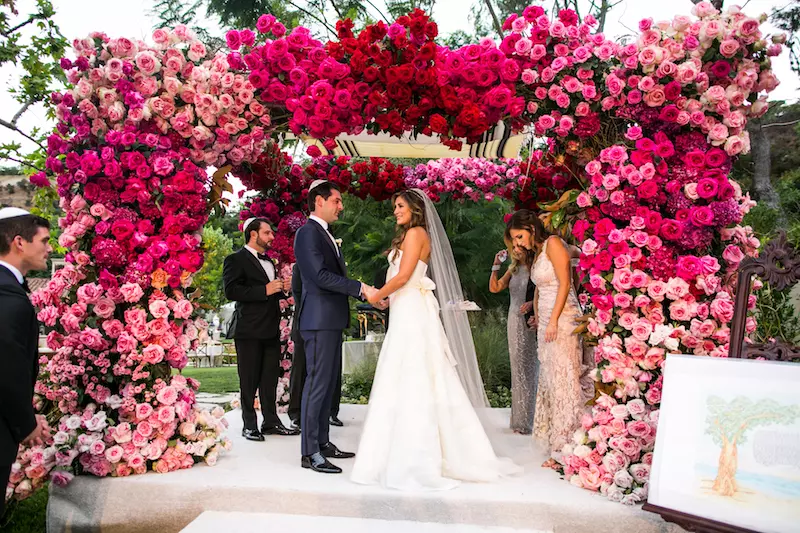 cerimonia de casamento judaico com casal abaixo da chupá florida com flores em tons de rosa