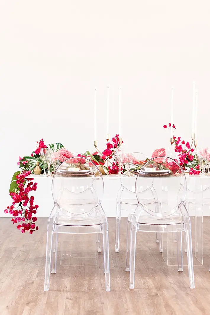 decoração de mesa de casamento minimalista com cadeiras de acrílico e arranjos florais tropicais de cor magenta