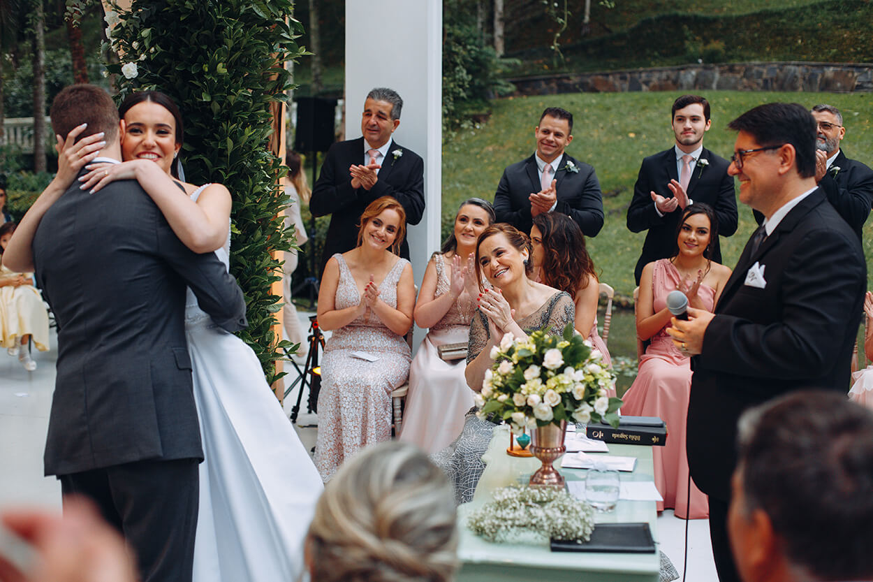 Convidados sorrindoe comemorando enquanto noivos se abraçam