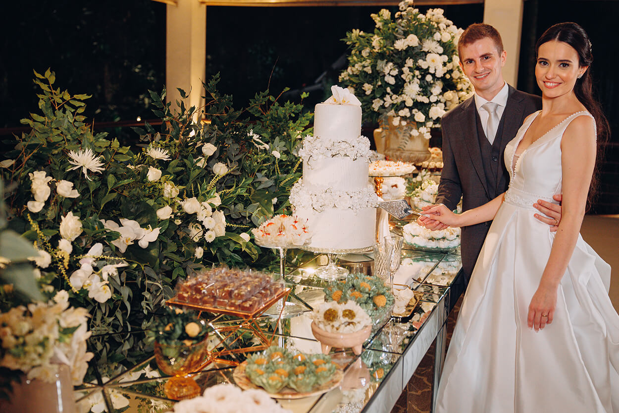 Noivos cortando o bolo de casamento clássico branco