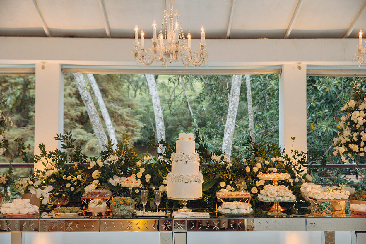 Mesa com o bolo de casamento enfeitada com folhas e flores branca
