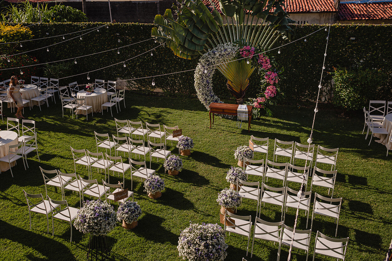 Vista de cima de cadeiras brancas de frente para o altar circular com metade com flores rosas e a outra metade com flores brancas 