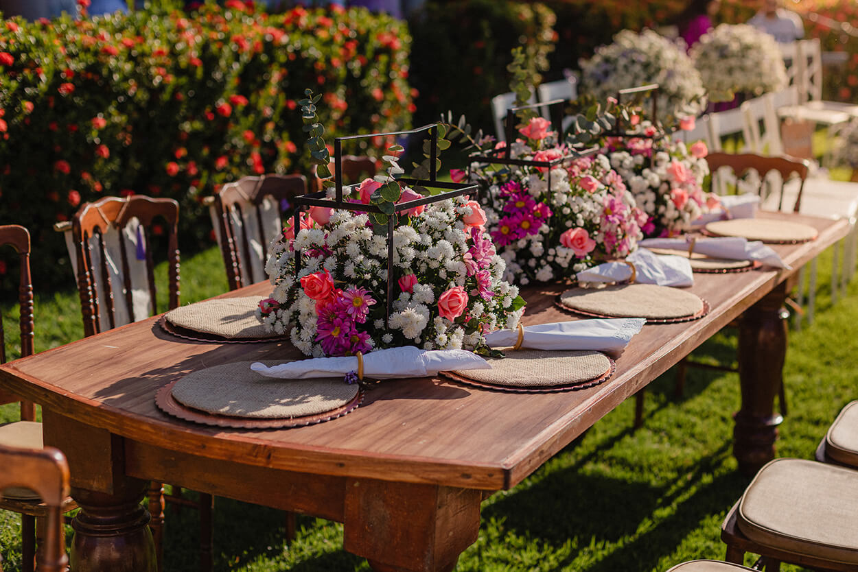 Mesa de madeira com flores brancas, rosas e lilás no centro da mesa