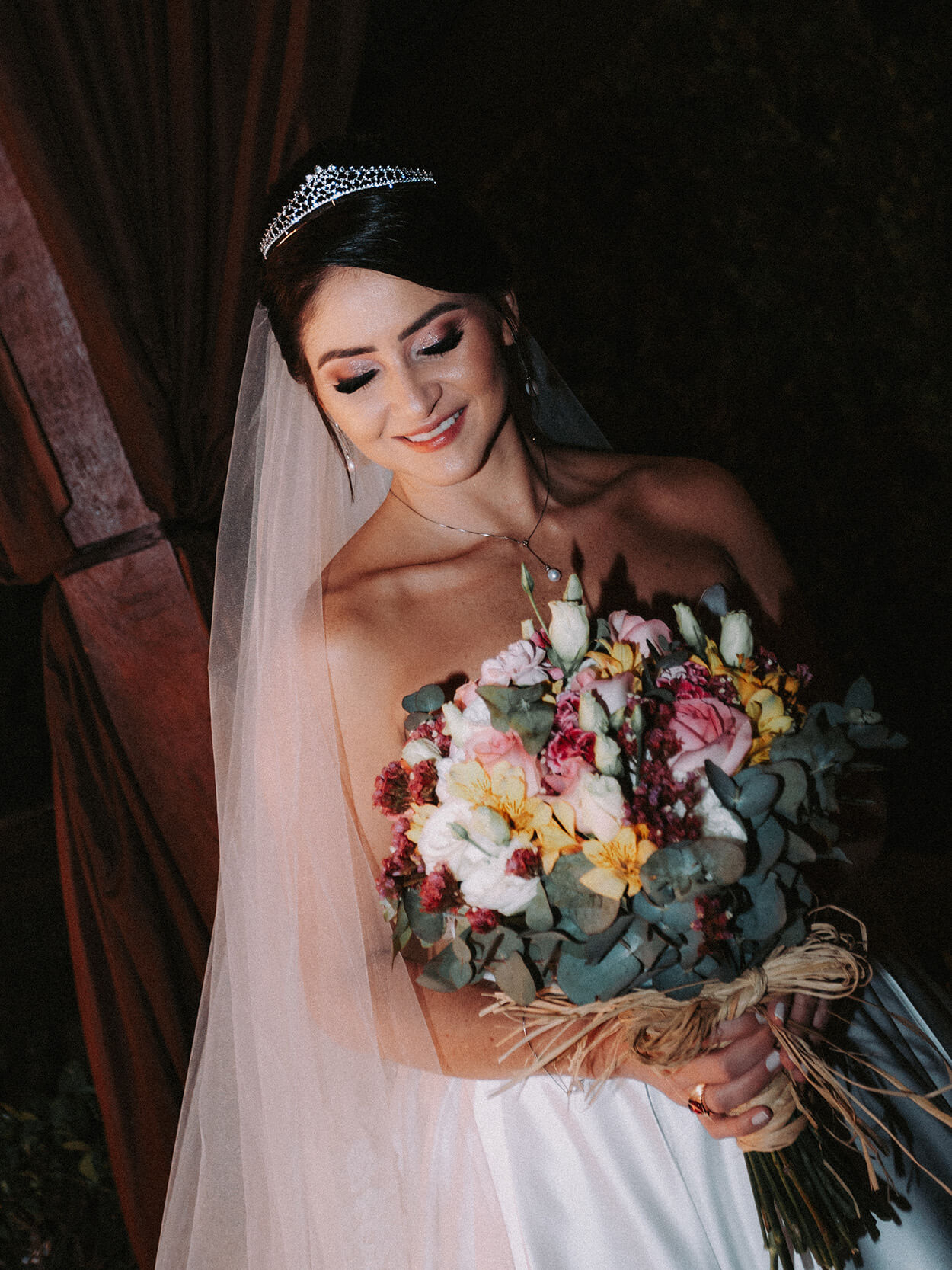 Noiva com véu segurando buquê com flores brancas, rosas, vermelhas e amarelas