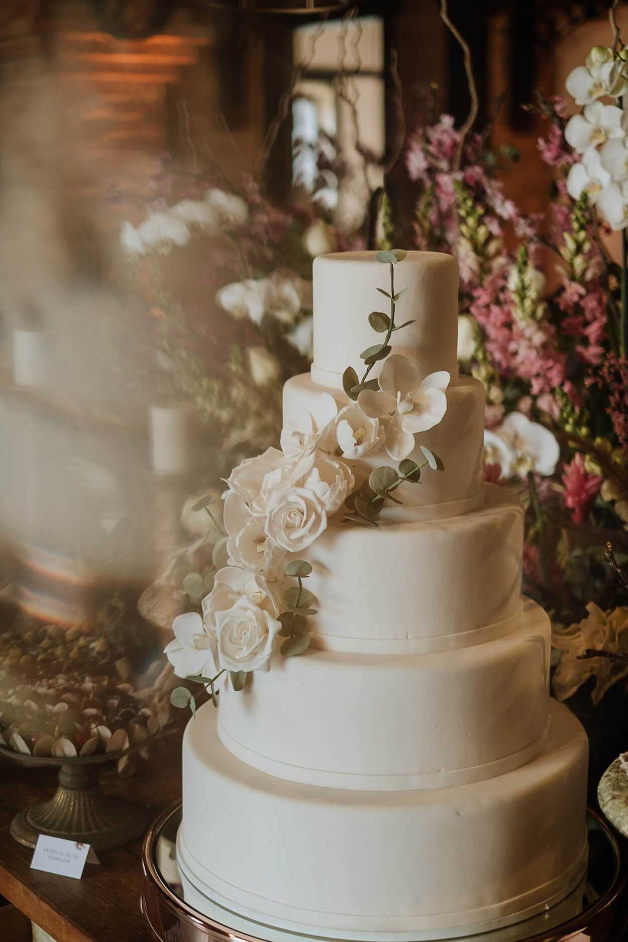 bolo de casamento branco redondo com cinco andares com topo de floral de rosas brancas e folhas de eucalipto