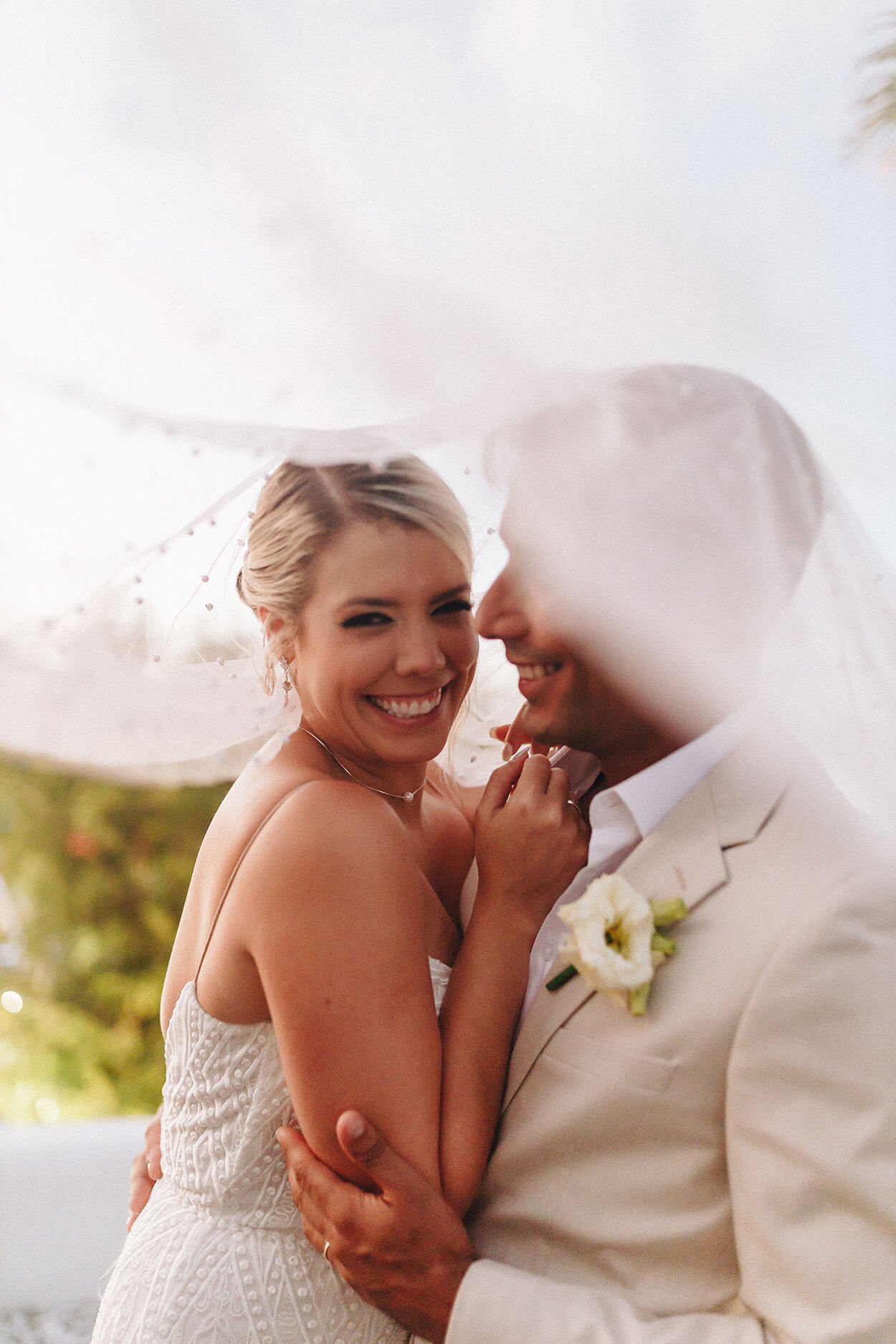 Noivos sorrindo debaixo do véu da noiva
