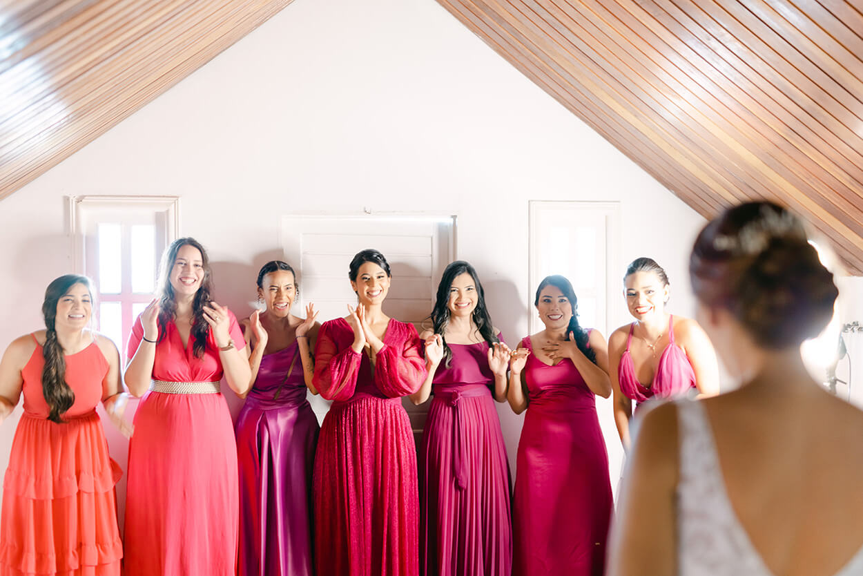 Mulheres com vestidos viva magenta e rosa dentro da sala vendo a noiva pela primeira vez