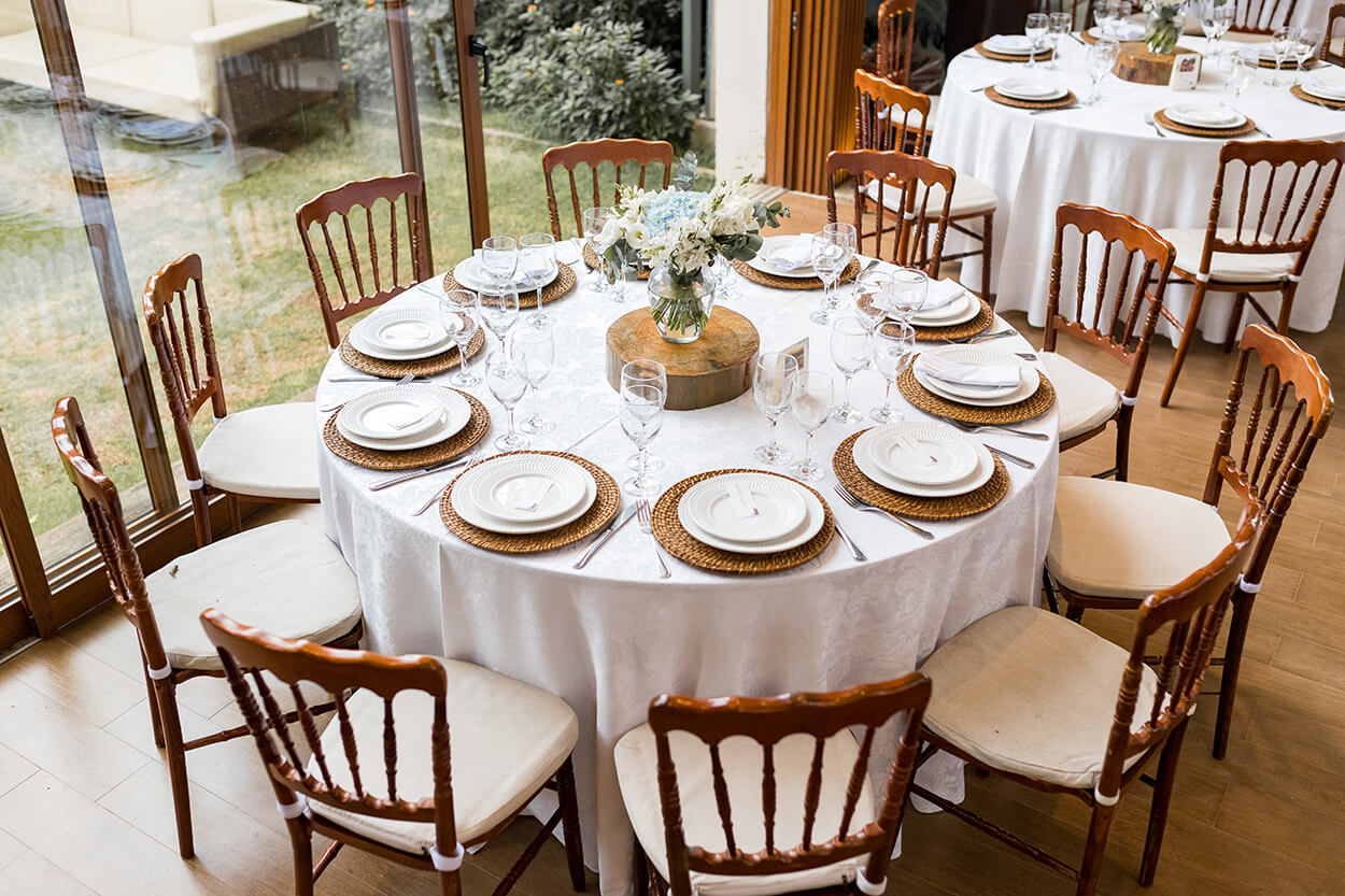 Mesa redonda com toalha branca e centro de mesa com vasos de flores brancas e azuis