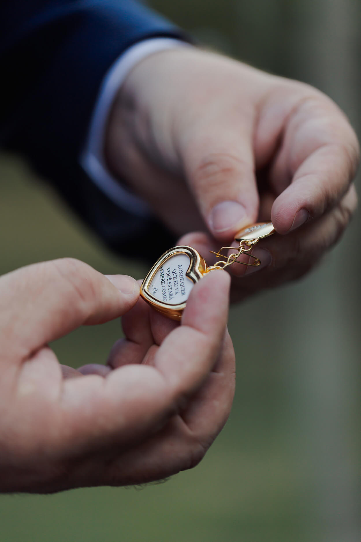 Mãos mascluinas segurando pequeno relicário dourado em formato de coração