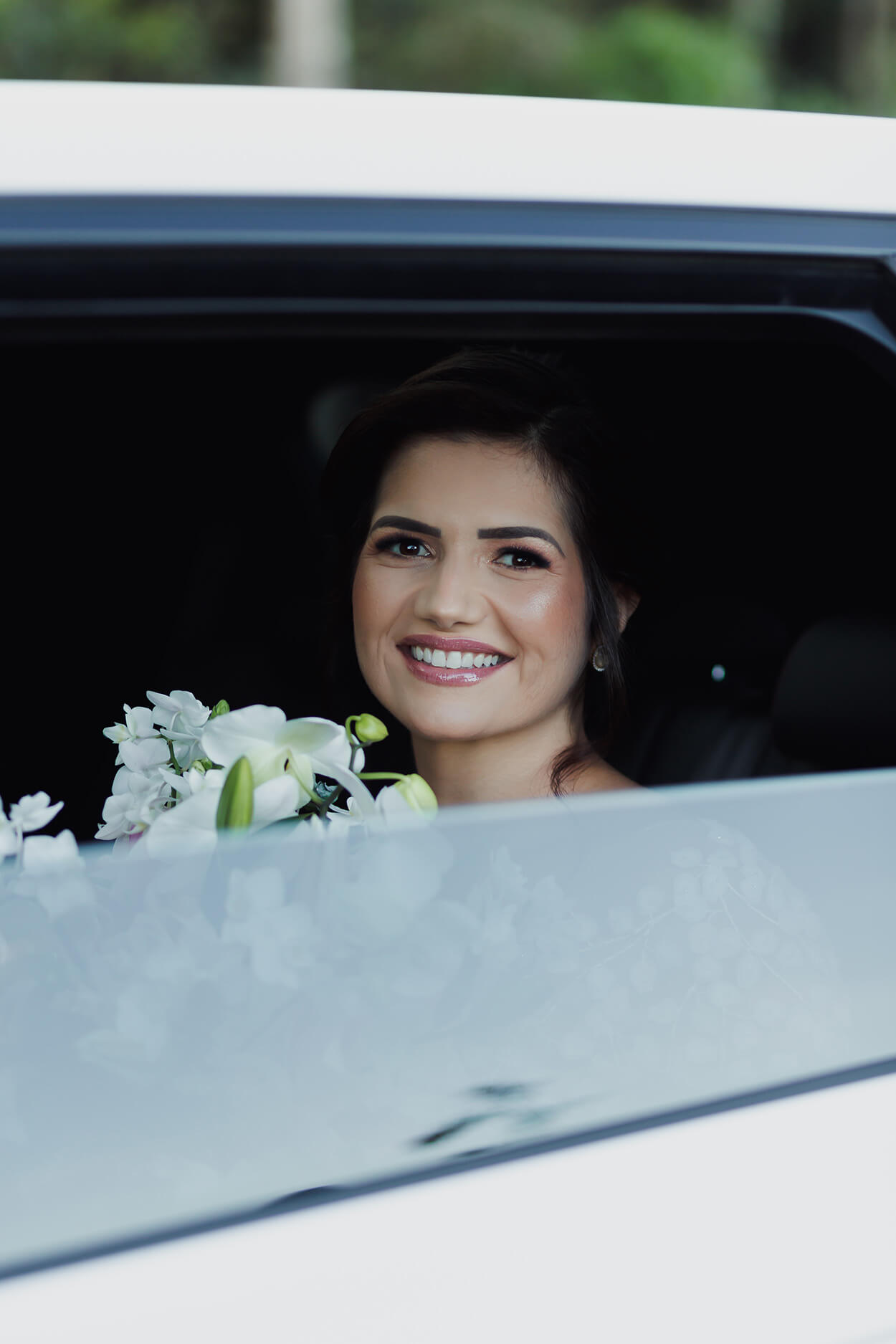 Noiva segurando o buquê e sorrindo dentro do carro