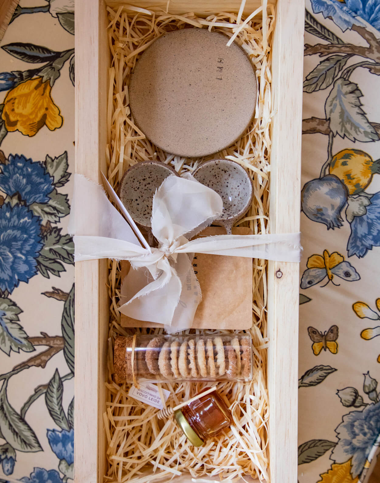 Caixa de madeira com laço branco para presente para os padrinhos contendo duas xícaras pequenas e pacote de bo lachas