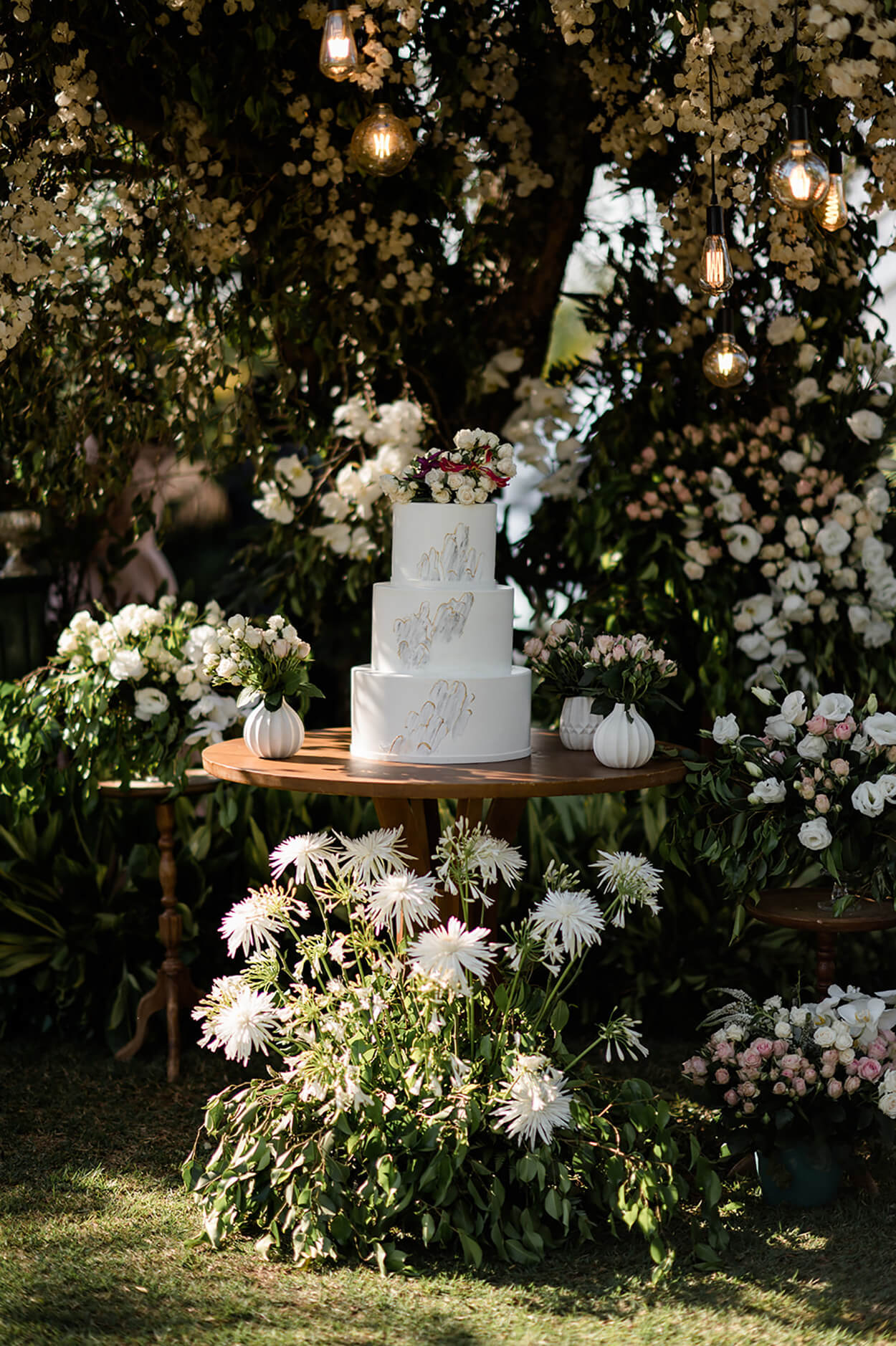 Mesa de madeira redonda com bolo de casamento branco com três andares