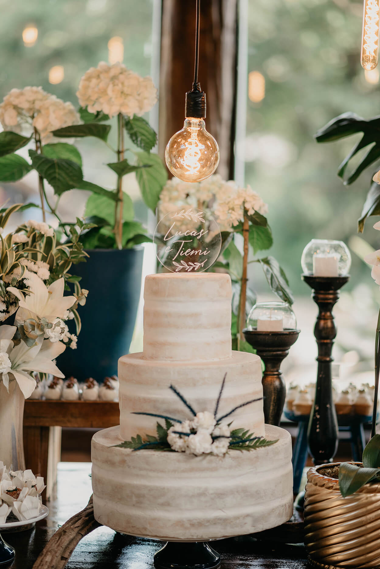 Bolo de casamento branco com três andares semi espatulado com flores brancas e topo com círculo em acrílico com o nome dos noivos