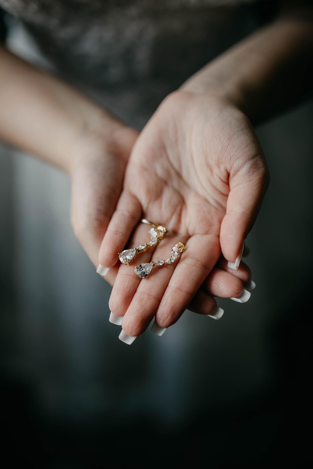 Mãos femininas segurando brincos dourados em formato de gota