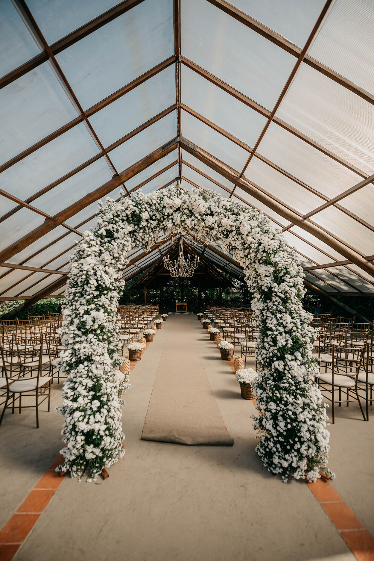 Arco com flores brancas e cadeiras madeira sob capela de cristal