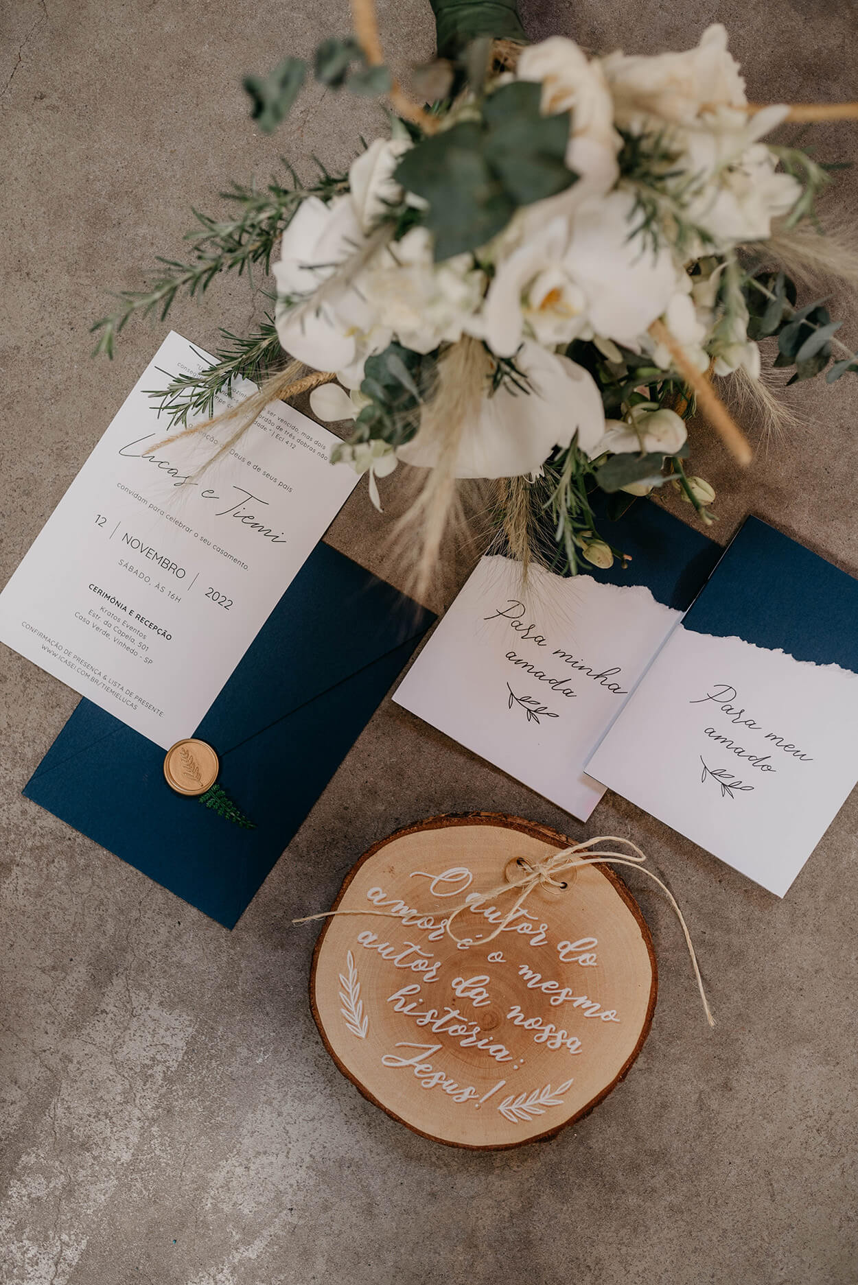 Convites de casamento branco e azul marinho ao lado de porta alianças em tora de madeira