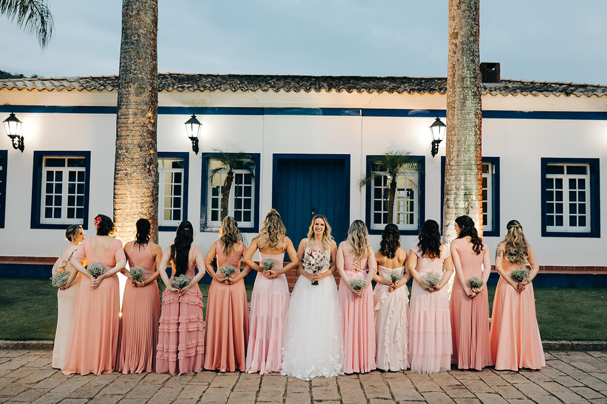 Madrinhas de costas segurando pequeno buquê mosquitinho com vestido rosa e noiva ao centro