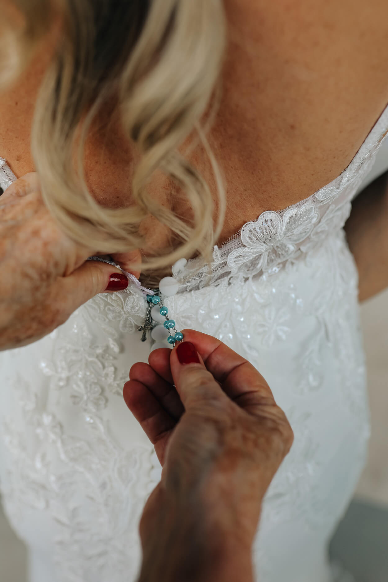 Mulher colocando mini terço no vetsido da noiva
