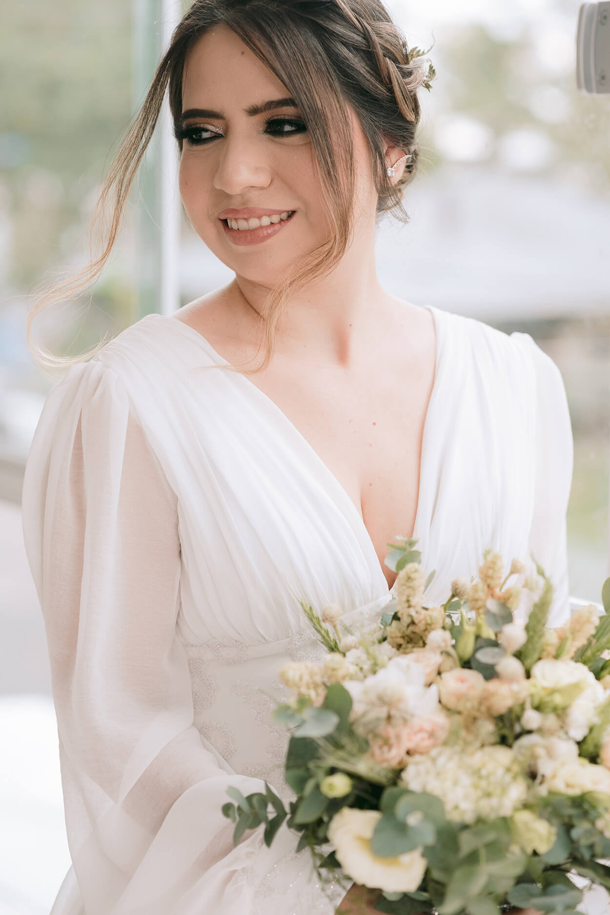 Noiva com vestido de noiva com decote em v e mangas transparentes segurando buquê