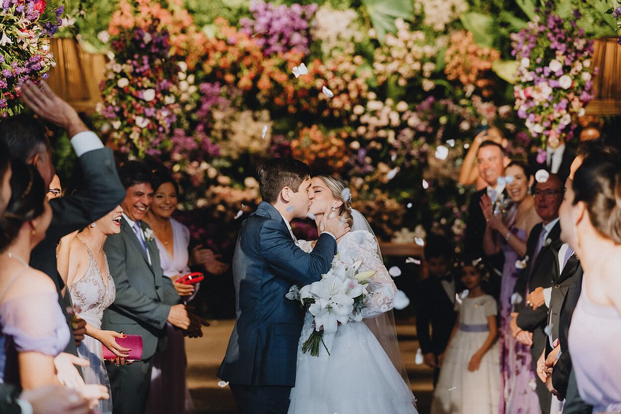Noivos se beijando na saída do casamento no salão