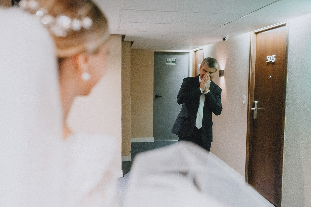 Pai d anoiva de terno preto no corredor emocionado ao ver a filha com vestido de noiva