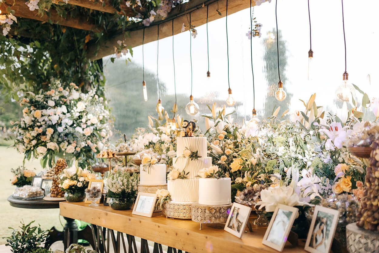 Mesa de madeira com trio de bolos e flores