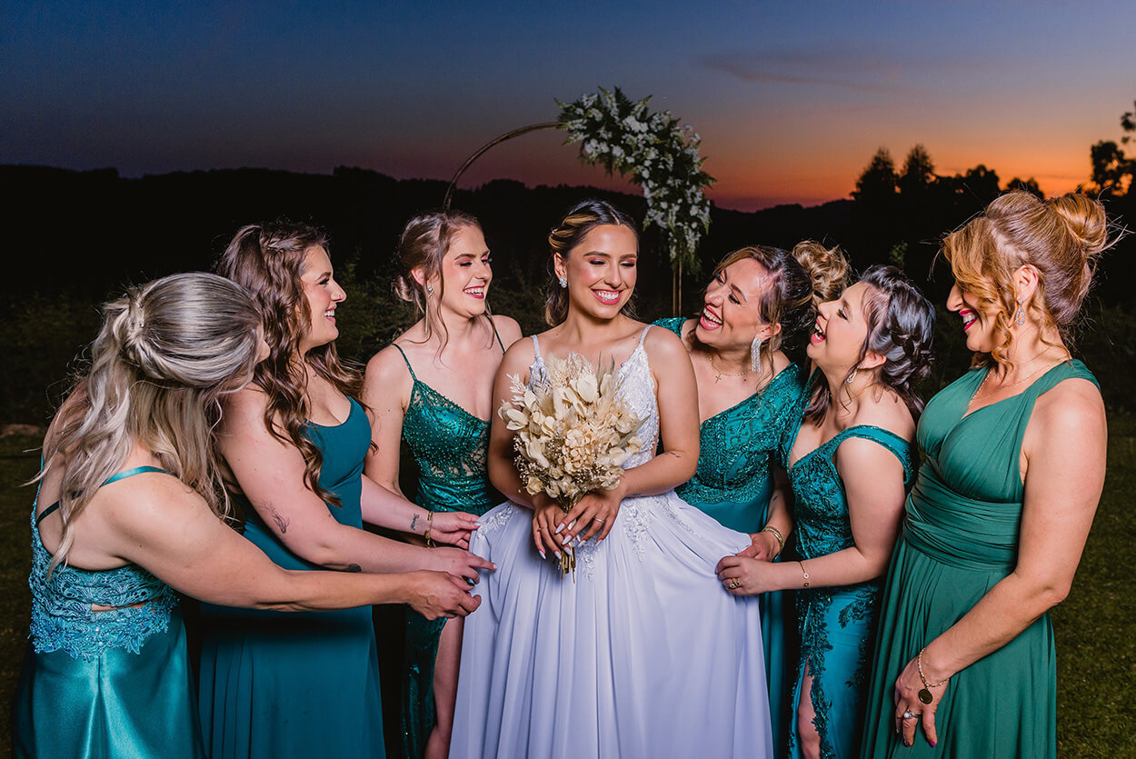 Madrinhas com vestido verde esmeralda em volta da noiva segurando um buquê com capim dos pampas ao pôr do sol