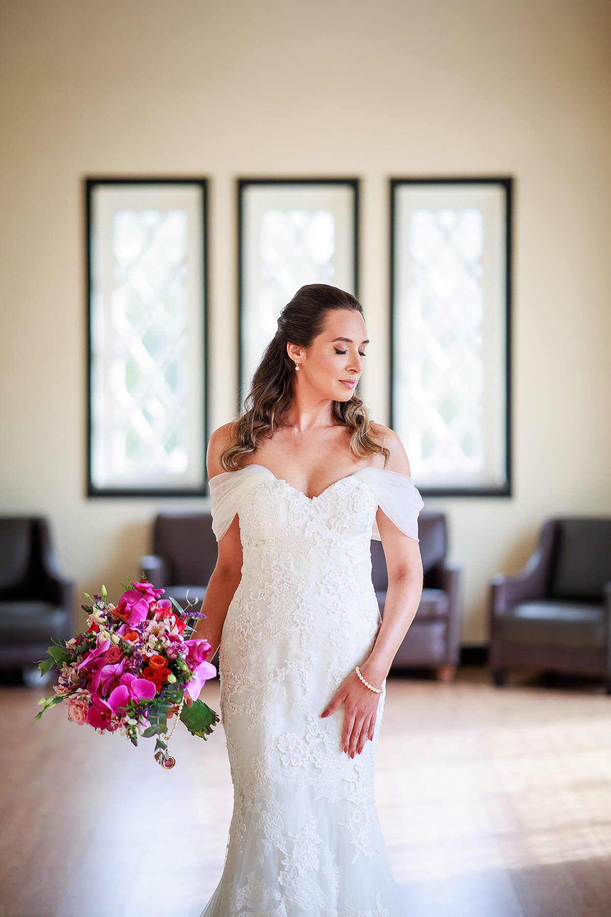 Mulher na sala com vestido de noiva com manga pendente segurando buquê com rosas e orquídeas rosas