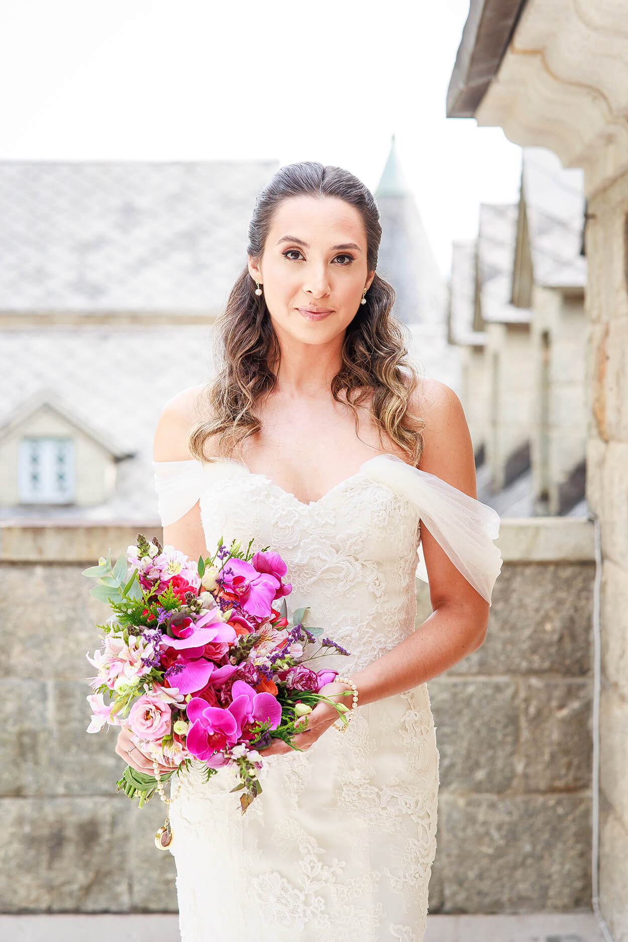 Mulher com vestido de noiva com manga pendente segurando buquê com rosas e orquídeas rosas