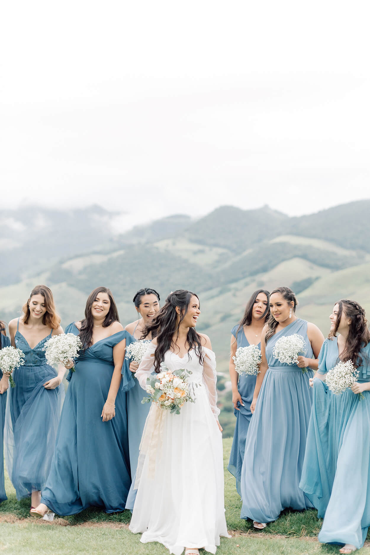 Noiva sorrindo olhando para as madrinhas usando vestidos azuis claro