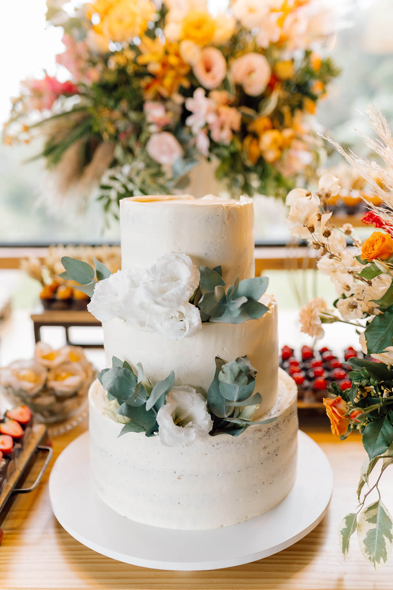 Bolo de casamento com três andares ramos de eucalipto e flores brancas
