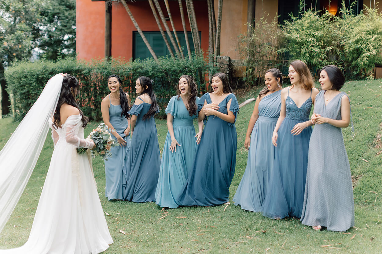 Madrinahs com vetsido azul reagindo ao first look com a noiva