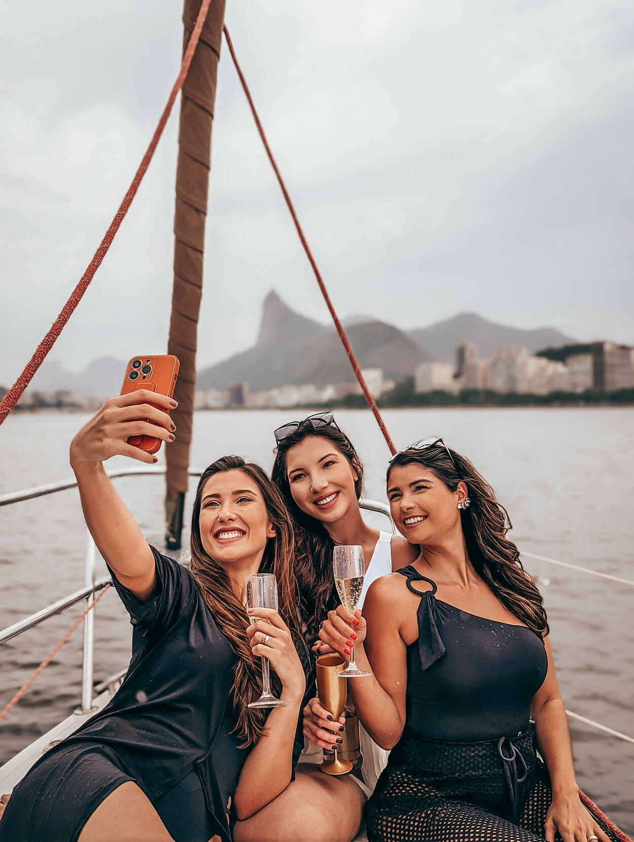 Três mulheres com taças brindando e fazendo selfie no veleiro