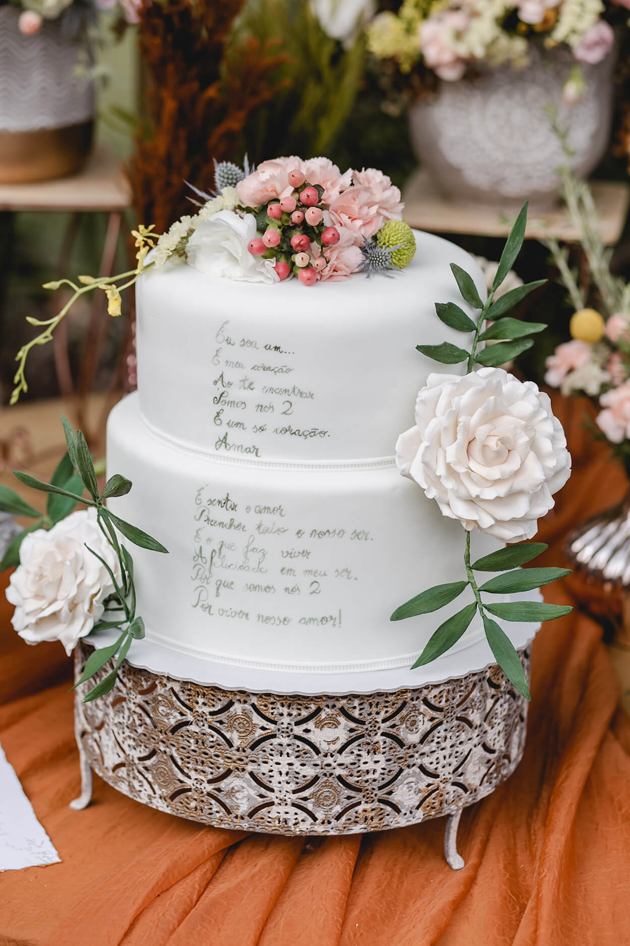 bolo de casamento de dois andares com poema escrito além de rosas e flores no topo