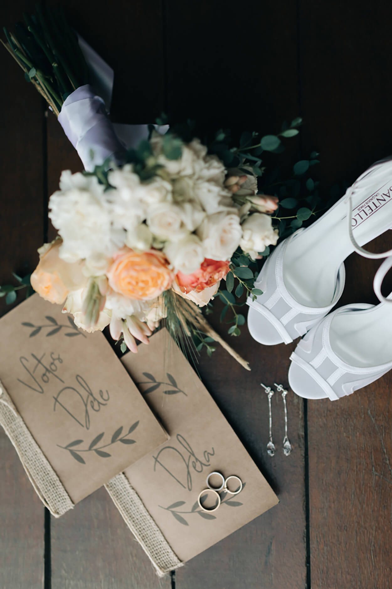 Buquê com flores brancas e laranjas ao lado de caderno de votos em papel kraft e sandalía branca