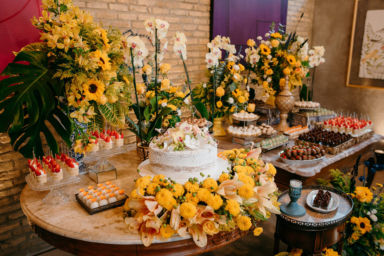 Mesa de madeira com bolo de casamento e flores amarelas