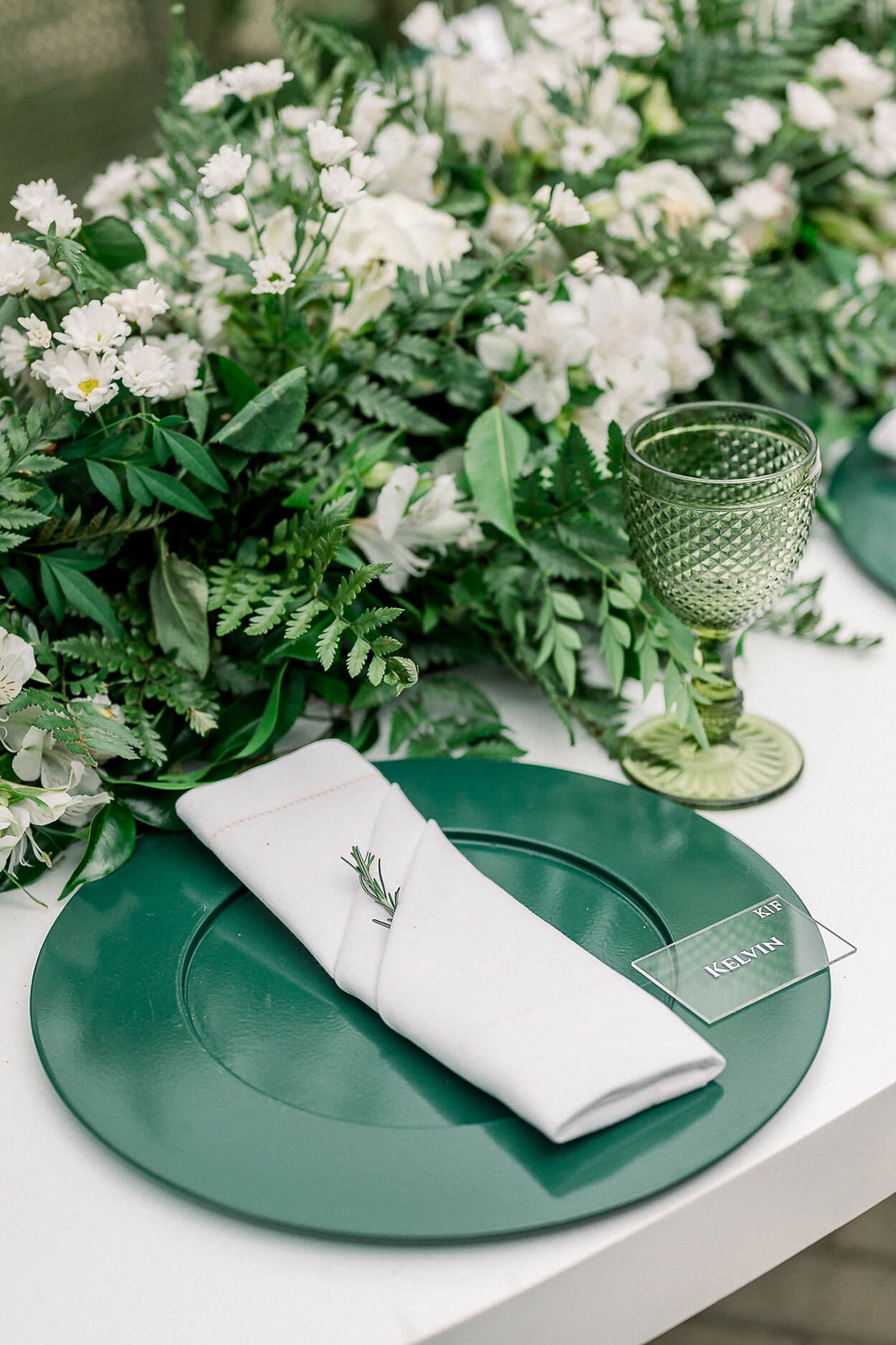 sousplat verde esmeralda com guardanapo branco e flores brancas ao centro