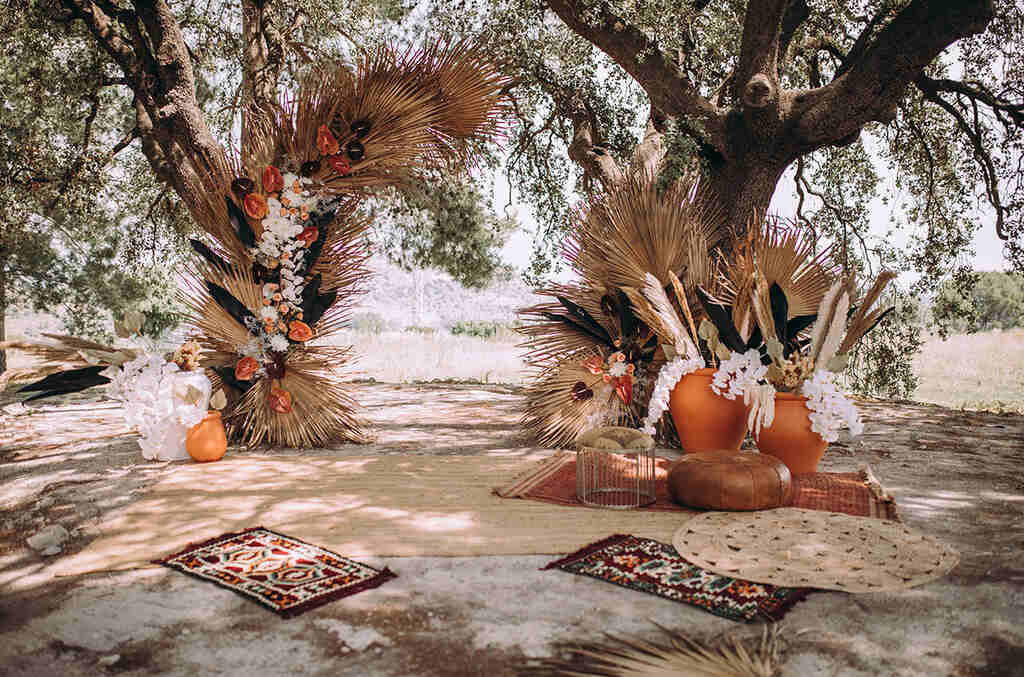 decoração de casamento ao ar livre no estilo boho com tapetes e árvores com folhagens secas