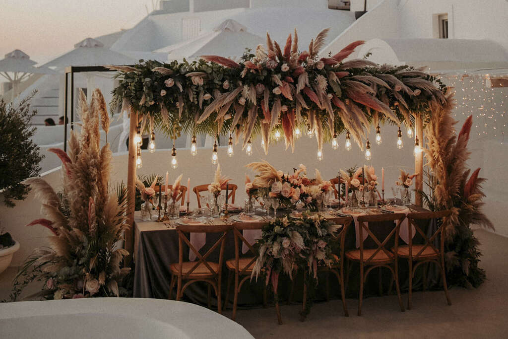 mesa para convidados com decoração de casamento com lâmpadas suspensas e folhagens secas robusta