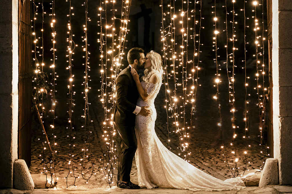 noivos se beijando com painel de varal de luzes para decoração de casamento