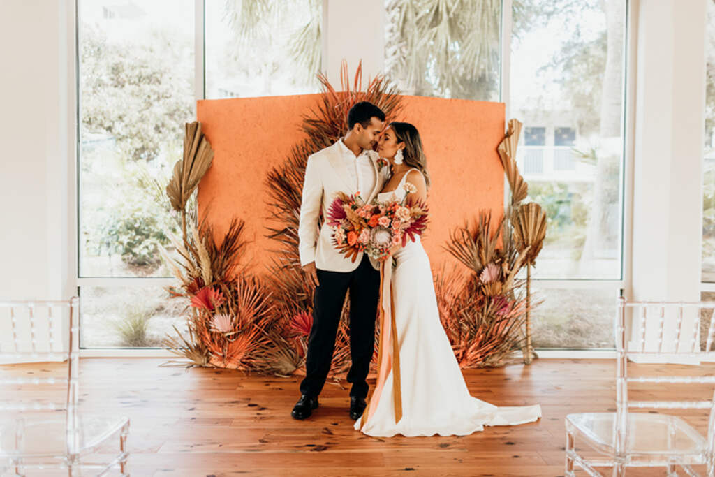 noivos em frente ao painel laranja com decoração de casamento folhas secas