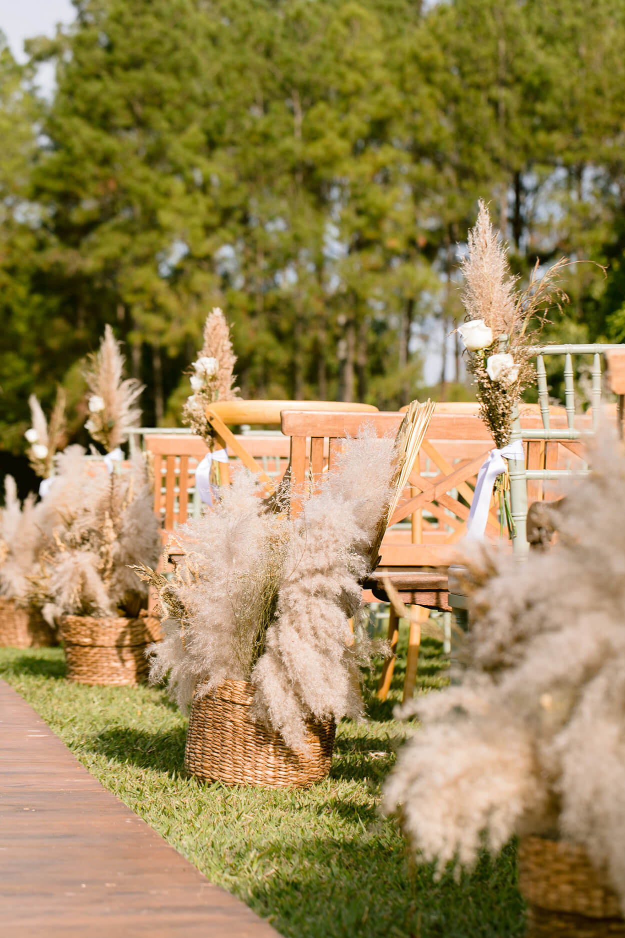Bancos e cadeiras de madeira clara e vasos com capim dos pampas no jardim de frente para o lago para realizar casamento